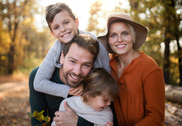 A beautiful young family with small children on a walk in autumn forest, looking at camera.