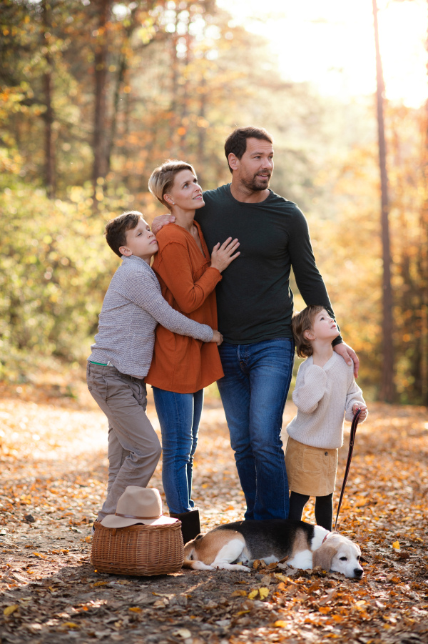 Portrait of beautiful young family with small children and dog standing in autumn forest.