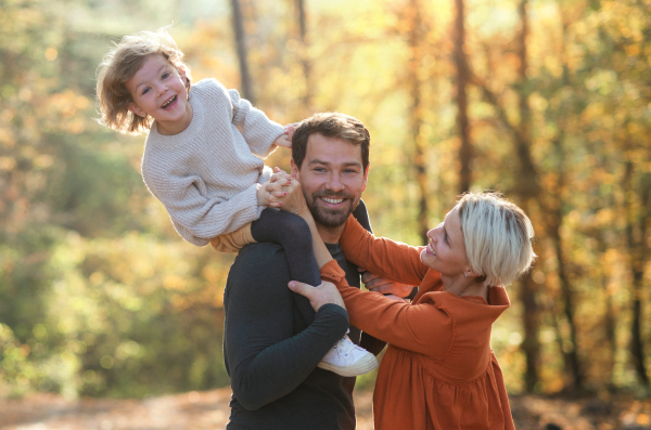 Beautiful young family with small daughter on a walk in autumn forest, having fun.