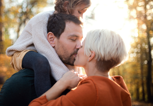 Beautiful young couple with small daughter on a walk in autumn forest, kissing.