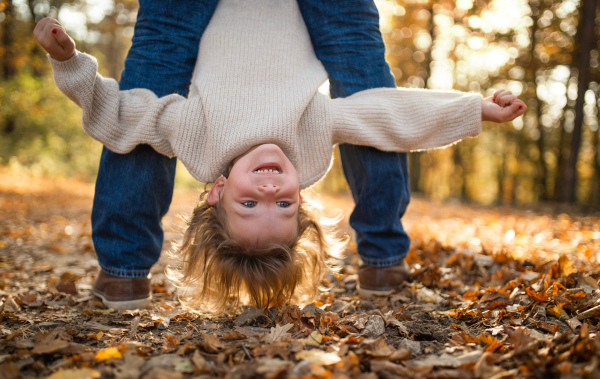 An unrecognizable father holding small daughter upside down in autumn forest.