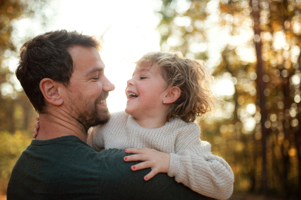 Mature father holding small daughter on a walk in autumn forest, having fun.