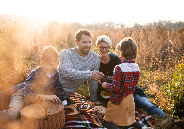 Beautiful young family with small children having picnic in autumn nature, sitting on grass.