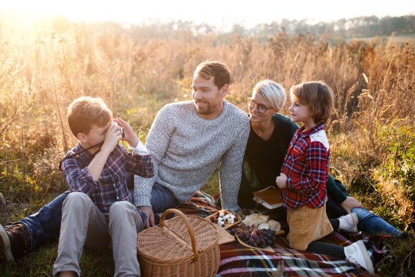 Beautiful young family with small children having picnic in autumn nature, taking photographs.