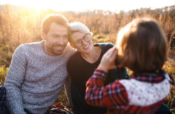 Portrait of small girl with family on picnic in autumn nature, taking photographs with camera.