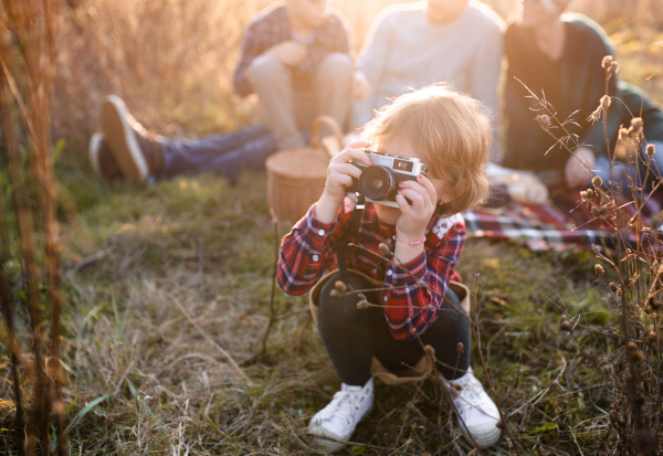 Portrait of small girl with family on picnic in autumn nature, taking photographs with camera.