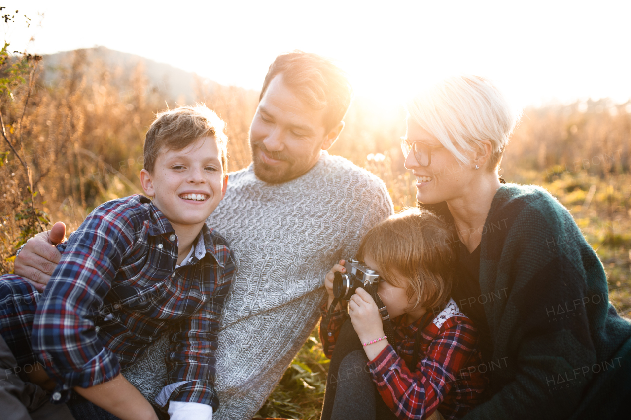 Portrait of small girl with family sitting in autumn nature, taking photographs with camera.