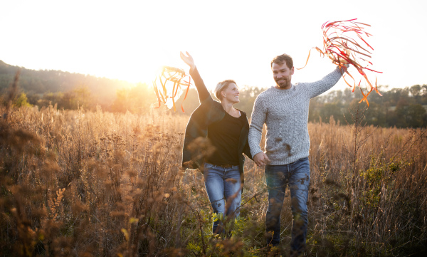 Front view of young couple in love on a walk in autumn forest, holding hand ribbon kites.