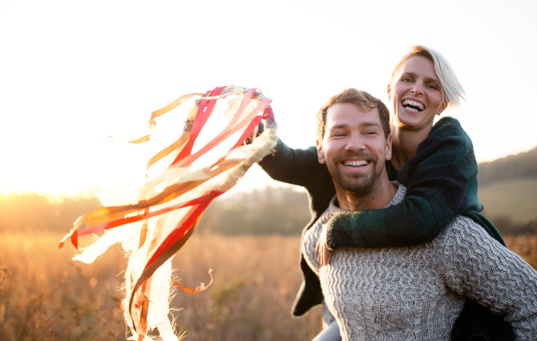 Happy young couple in love on a walk in autumn forest, holding hand ribbon kites.