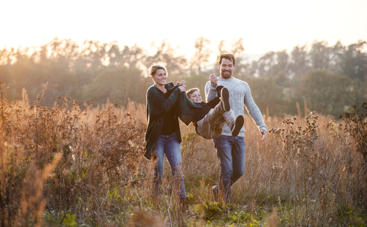 Beautiful young family with small son on a walk in autumn nature, having fun.