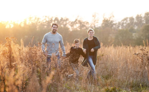 Beautiful young family with small son on a walk in autumn nature, having fun.