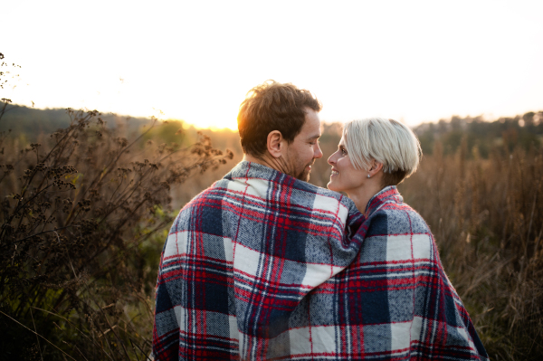 Rear view of young couple in love on a walk in autumn nature at sunset.