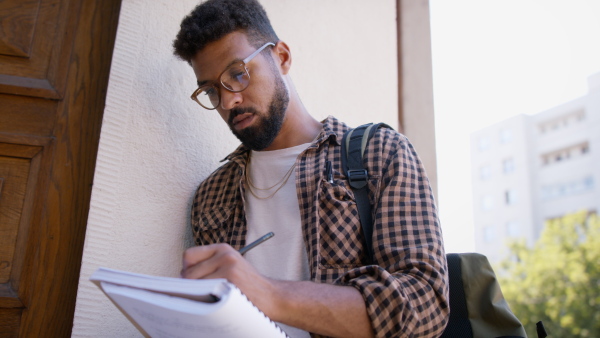 Young african-american student preparing for exam in front of the university building.