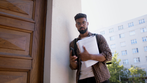 Young african-american student preparing for exam in front of the university building, looking at camera.