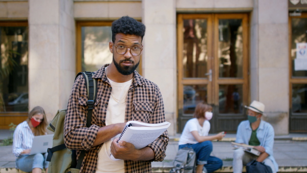 Young african-american student preparing for exam in front of the university building.