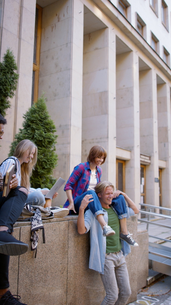 A vertical footage of group of students meeting in front of the university building, young couple doing piggy back ride.