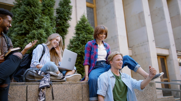 A group of students meeting in front of the university building, young couple doing piggy back ride.