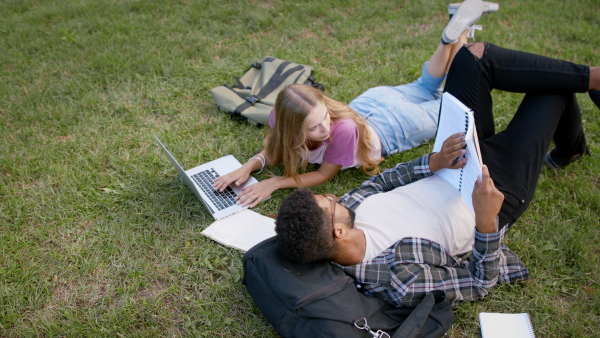 Young student couple in park, talking and working on school project.