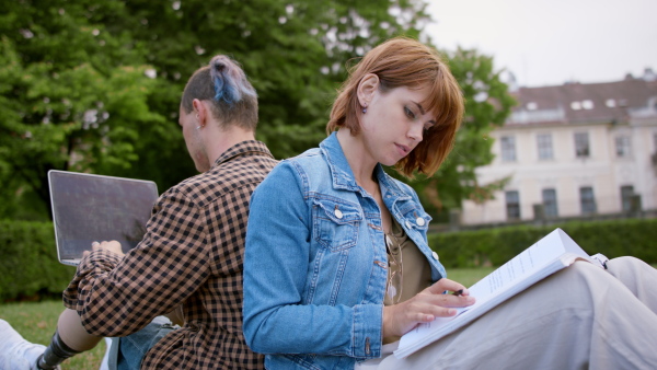 Young student couple sitting in park, working on school project, leg prosthetic concept.