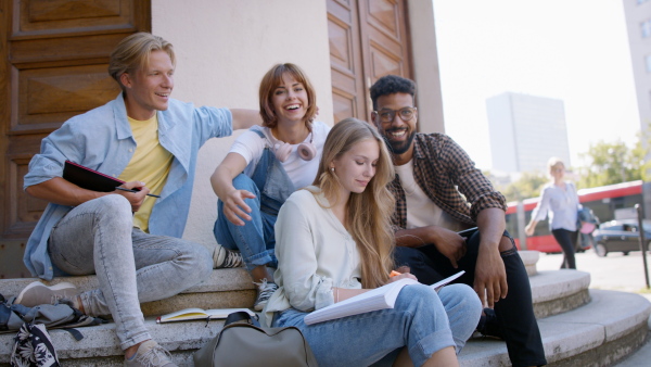 A group of students sitting on staircase, working school project and looking at camera.