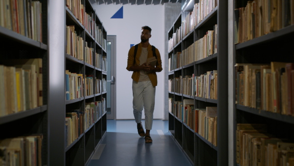 A young african-american male student looking for books in university library.