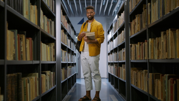 A young african-american male student standing and looking at camera in university library.