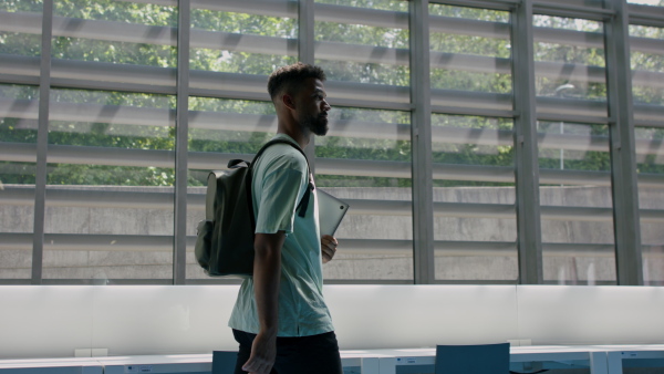 Young african-american male university student walking through corridor indoors, looking around.