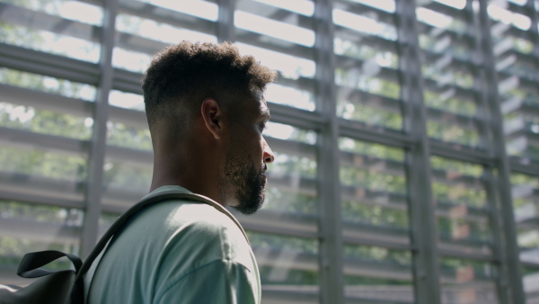 Young african-american male university student walking through corridor indoors, looking around.