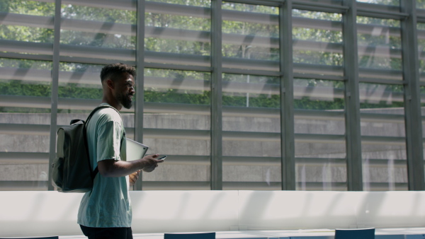 Young african-american male university student walking through corridor indoors, greeting other student.