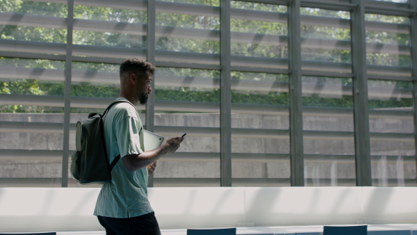 Young african-american male university student walking through corridor indoors, greeting other student.