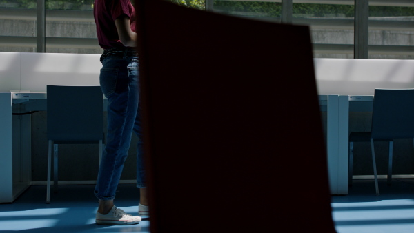 A mid-section of young female university student walking through corridor indoors.