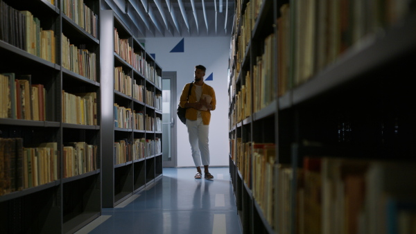 A young african-american male student looking for books in university library.