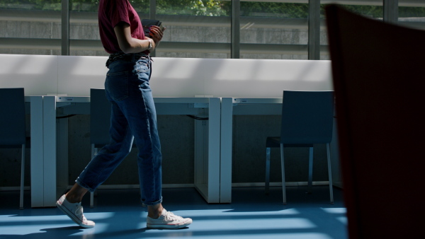 A mid-section of young female university student walking through corridor indoors.