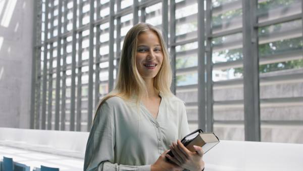 A young female university student standing in corridor indoors, looking at camera.