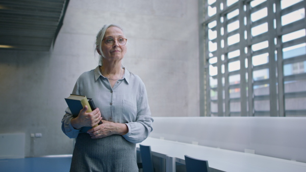 A senior female university teacher walking through corridor indoors, looking around.