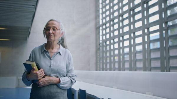 A senior female university teacher walking through corridor indoors, looking at camera.