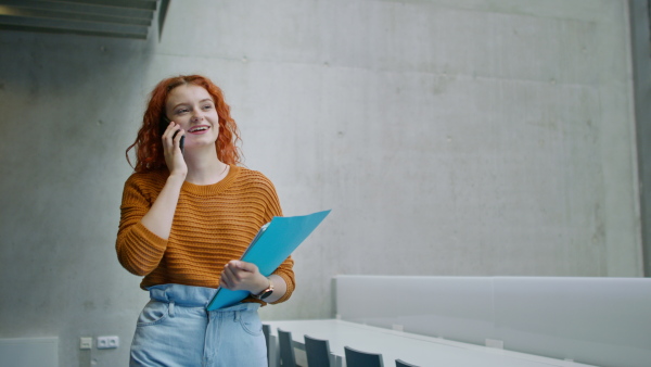 A young female university student walking through corridor indoors, having a call.