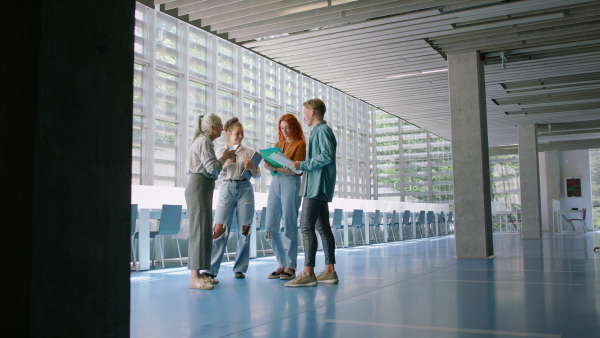 A group of university students with teacher standing in corridor indoors, talking.