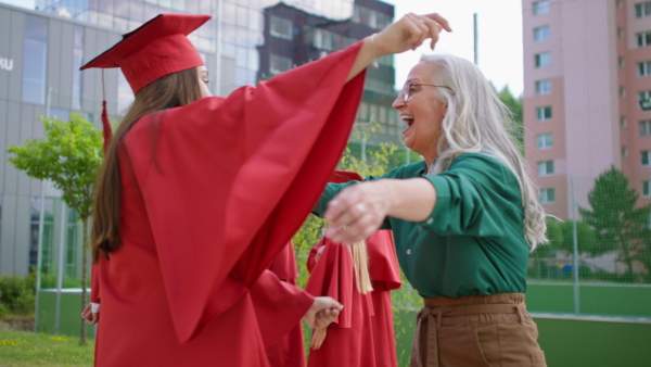 A cheerful university student celebrating with mother outdoors, graduation concept.