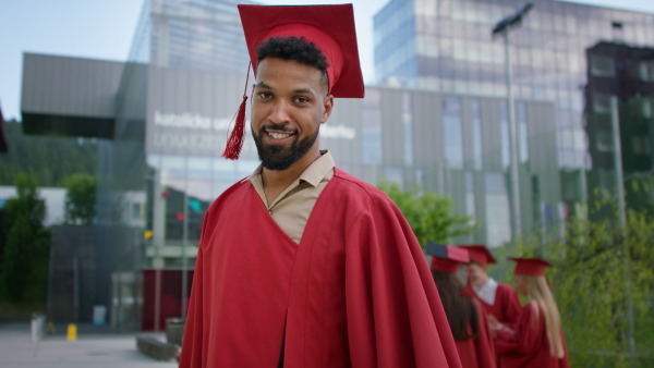 Portrait of happy university student with hat and gown looking at camera outdoors, graduation concept.