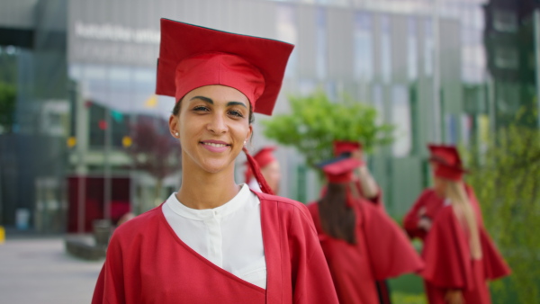 Front view of happy university student with hat and gown looking at camera outdoors, graduation concept.