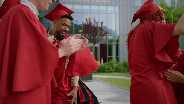 A group of cheerful university students dancing and celebrating outdoors, graduation concept.