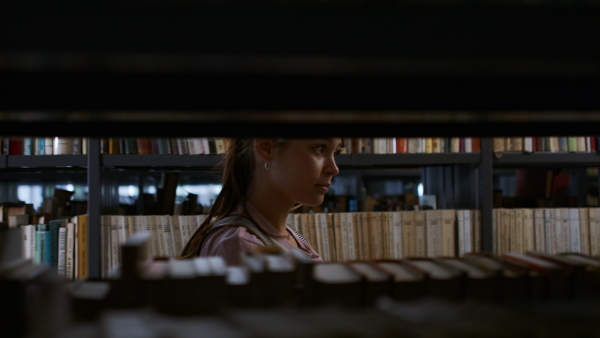 A young female student looking for books in university library.