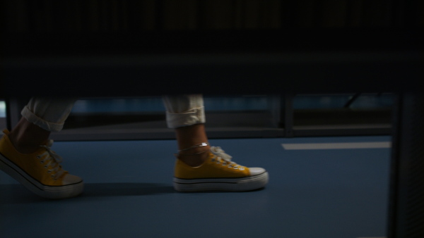 A side view of young female student looking for books in university library, close up on feet.