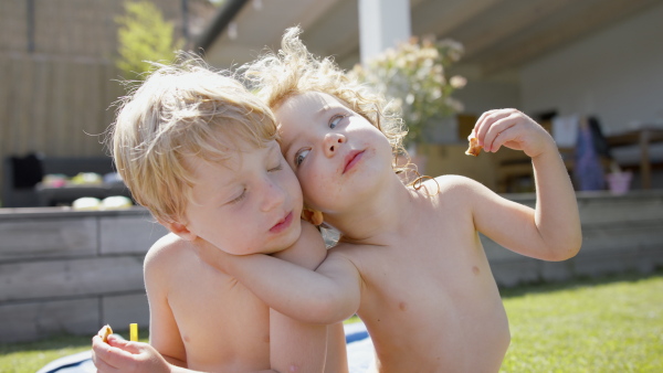 A front view of two sibling in swimsuit sitting next to pool and looking at camera.