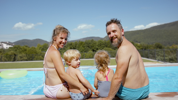 A rear view of beautiful family sitting on the edge of the pool and having fun together.