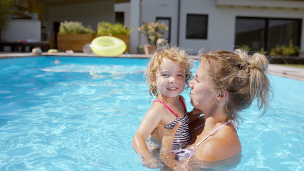 A beautiful family having fun together in the pool, looking at camera.