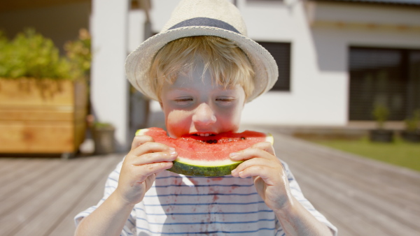 A close up of little boy eating a watermelon outside on terrace.