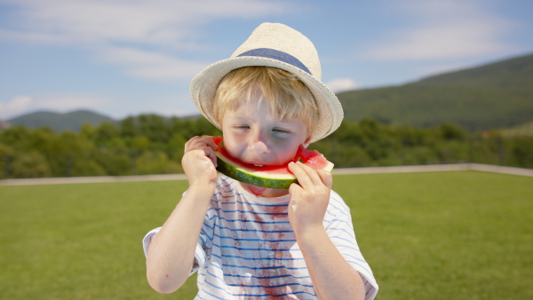 A close up of little boy eating a watermelon outside on terrace.