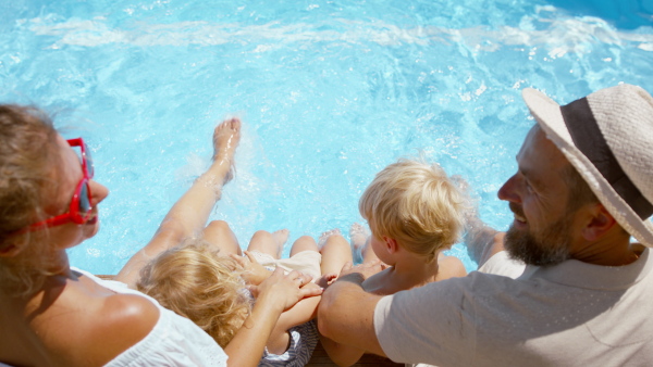 A top view of beautiful family sitting on the edge of the pool and having fun together.